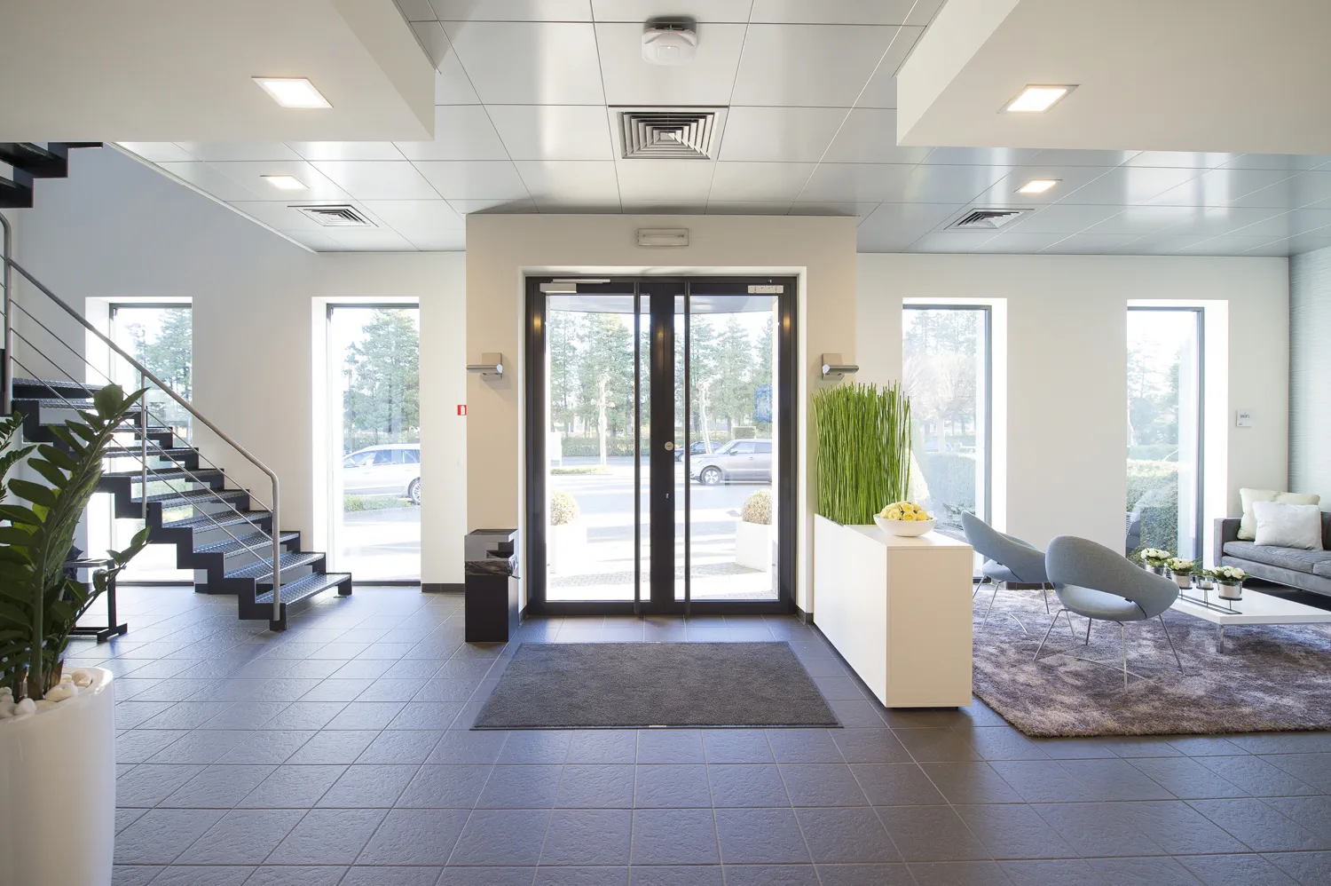 Inkomhal met grote glazen deur en wachtruimte met grijze stoelen